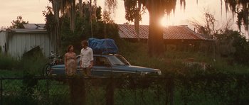 Movie still from “Away We Go” (2009), directed by Sam Mendes – A man and a woman walking next to an old car; Wide shot, Low angle