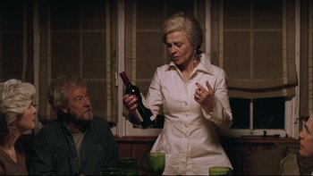 Movie still from “Away from Her” (2006), directed by Sarah Polley – An older woman holding a bottle of wine while standing next to an older man; Medium shot, Over the shoulder angle