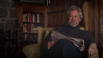 Movie still from “Away from Her” (2006), directed by Sarah Polley – An older man sitting in a chair reading a newspaper; Medium shot, Over the shoulder angle