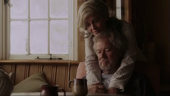Movie still from “Away from Her” (2006), directed by Sarah Polley – An older man and a younger woman sitting in front of a coffee mug; Medium shot, Low angle