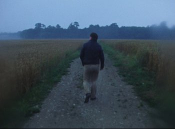 Movie still from “Baal” (1970), directed by Volker Schlöndorff – A man walking down a dirt road near a field; Wide shot, High angle