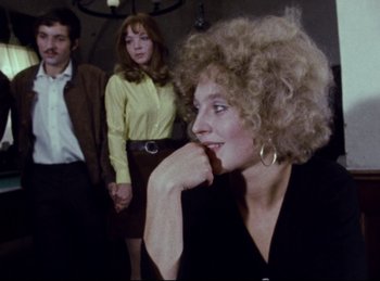 Movie still from “Baal” (1970), directed by Volker Schlöndorff – A woman sitting in front of two other people; Medium shot, Over the shoulder angle