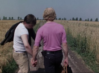 Movie still from “Baal” (1970), directed by Volker Schlöndorff – Two men walking down a dirt road holding hands; Medium shot, High angle