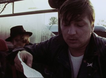 Movie still from “Baal” (1970), directed by Volker Schlöndorff – A man sitting on top of a bus while holding a piece of paper in his hand; Close Up shot, Low angle