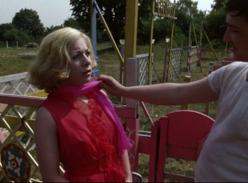 Movie still from “Baal” (1970), directed by Volker Schlöndorff – A woman in a red dress tying a pink scarf around a woman's neck; Medium shot, Over the shoulder angle