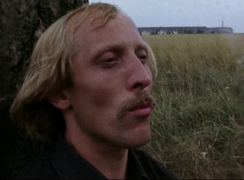 Movie still from “Baal” (1970), directed by Volker Schlöndorff – A person in a field near a tree; Close Up shot, Low angle