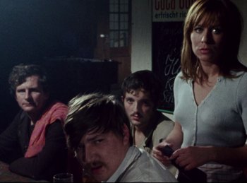 Movie still from “Baal” (1970), directed by Volker Schlöndorff – A group of people sitting at a table in front of a chalkboard; Medium shot, Low angle