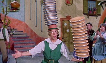 Movie still from “Babes in Toyland” (1961), directed by Jack Donohue – A man in a green suit and a hat is balancing plates on his head; Medium shot, Low angle