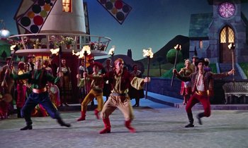 Movie still from “Babes in Toyland” (1961), directed by Jack Donohue – A group of people in costumes holding torches in front of an audience; Wide shot, Low angle