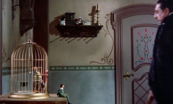 Movie still from “Babes in Toyland” (1961), directed by Jack Donohue – A room with a bird cage and a man sitting on a chair; Wide shot, High angle