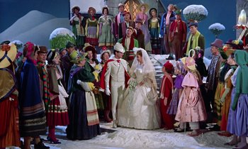 Movie still from “Babes in Toyland” (1961), directed by Jack Donohue – A group of people standing around a bride and groom in front of a crowd; Wide shot, High angle