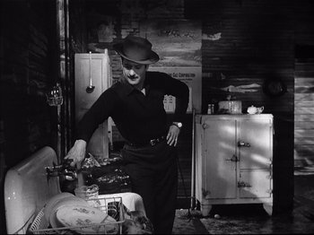Movie still from “Baby Doll” (1956), directed by Elia Kazan – A man standing in front of an old fashioned stove; Medium shot, High angle