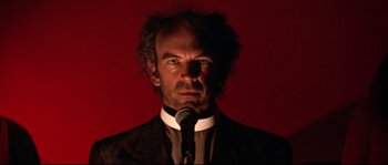A man in a suit and tie holding a microphone in front of a red background