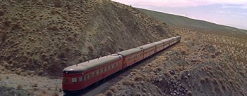 Movie still from “Bad Day at Black Rock” (1955), directed by John Sturges – A train traveling down tracks next to a mountain side; Extreme Wide shot, High angle