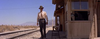 Movie still from “Bad Day at Black Rock” (1955), directed by John Sturges – A man standing on the side of a train track next to a building; Wide shot, Low angle