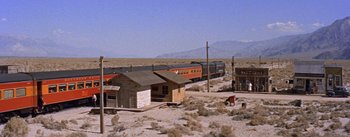 Movie still from “Bad Day at Black Rock” (1955), directed by John Sturges – A train traveling down train tracks next to buildings; Extreme Wide shot, High angle
