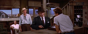 Movie still from “Bad Day at Black Rock” (1955), directed by John Sturges – An older man smoking a cigarette while sitting at a table; Medium shot, Over the shoulder angle