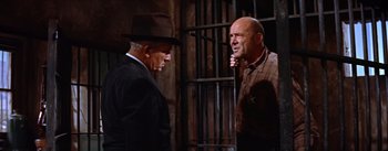 Movie still from “Bad Day at Black Rock” (1955), directed by John Sturges – Two men in suits and hats talking to each other in front of a metal gate; Medium shot, Low angle
