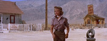 Movie still from “Bad Day at Black Rock” (1955), directed by John Sturges – A woman standing on a dirt road wearing a plaid shirt; Medium shot, Low angle
