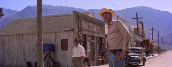 Movie still from “Bad Day at Black Rock” (1955), directed by John Sturges – A man in a cowboy hat standing in front of a bar and grill; Wide shot, Low angle
