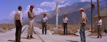Movie still from “Bad Day at Black Rock” (1955), directed by John Sturges – A group of men standing next to each other on the side of a road; Wide shot, Low angle