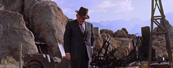 Movie still from “Bad Day at Black Rock” (1955), directed by John Sturges – An older man in a suit and hat standing in front of a pile of rocks; Wide shot, Low angle