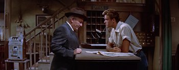 Movie still from “Bad Day at Black Rock” (1955), directed by John Sturges – A man in a suit and a man in a hat talking to each other in front of a desk; Medium shot, Low angle