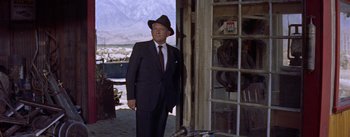 Movie still from “Bad Day at Black Rock” (1955), directed by John Sturges – A man in a suit and hat standing in front of a building; Medium shot, Low angle