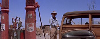 Movie still from “Bad Day at Black Rock” (1955), directed by John Sturges – An older man pumping gas into an old car; Wide shot, Over the shoulder angle