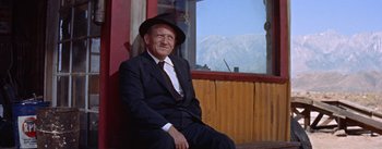 Movie still from “Bad Day at Black Rock” (1955), directed by John Sturges – An older man in a suit and hat sitting in front of a window; Medium shot, Low angle