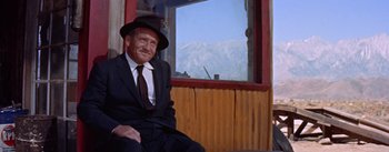 Movie still from “Bad Day at Black Rock” (1955), directed by John Sturges – An older man sitting in front of a window with mountains in the background; Medium shot, Low angle