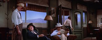 Movie still from “Bad Day at Black Rock” (1955), directed by John Sturges – A group of men sitting in chairs in a room with a mountain in the background; Wide shot, Low angle
