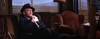 Movie still from “Bad Day at Black Rock” (1955), directed by John Sturges – A man sitting in a chair wearing a suit and hat; Medium shot, Low angle
