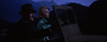 Movie still from “Bad Day at Black Rock” (1955), directed by John Sturges – A man and a woman sitting next to each other in front of mountains; Medium shot, Low angle