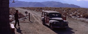 Movie still from “Bad Day at Black Rock” (1955), directed by John Sturges – An old car driving down a dirt road near mountains; Extreme Wide shot, High angle