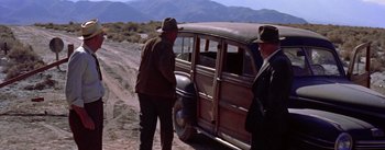 Movie still from “Bad Day at Black Rock” (1955), directed by John Sturges – Two men standing next to an old wooden car; Wide shot, High angle