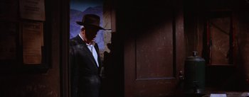 Movie still from “Bad Day at Black Rock” (1955), directed by John Sturges – A man in a suit and hat standing in front of an open door; Wide shot, Low angle