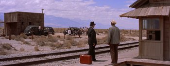 Movie still from “Bad Day at Black Rock” (1955), directed by John Sturges – Two men are standing on a train track near a train; Extreme Wide shot, Over the shoulder angle