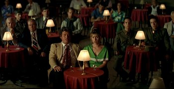 Movie still from “Bad Education” (2004), directed by Pedro Almodóvar – A group of people sitting around a table with lamps; Wide shot, High angle