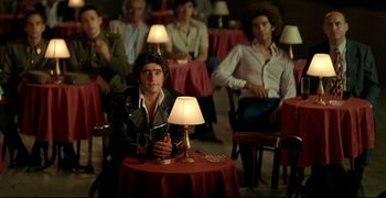Movie still from “Bad Education” (2004), directed by Pedro Almodóvar – A group of people sitting around a table with a lamp; Medium shot, Over the shoulder angle