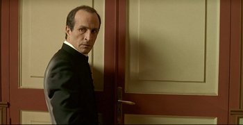 Movie still from “Bad Education” (2004), directed by Pedro Almodóvar – A man standing in front of a door wearing a suit and tie; Close Up shot, Over the shoulder angle