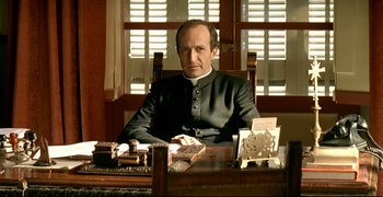 Movie still from “Bad Education” (2004), directed by Pedro Almodóvar – A man sitting at a desk in a room; Medium shot, Low angle