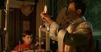 Movie still from “Bad Education” (2004), directed by Pedro Almodóvar – A priest is lighting candles for a young boy; Medium shot, Low angle