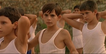 Movie still from “Bad Education” (2004), directed by Pedro Almodóvar – A young boy standing in front of a group of young people; Medium shot, Low angle