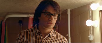 Movie still from “Bad Education” (2004), directed by Pedro Almodóvar – A man with long brown hair wearing glasses and a striped shirt; Close Up shot, Low angle