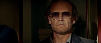 Movie still from “Bad Education” (2004), directed by Pedro Almodóvar – A person wearing a suit and sunglasses; Close Up shot, Low angle