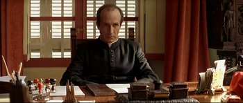 Movie still from “Bad Education” (2004), directed by Pedro Almodóvar – A man sitting at a table in front of papers; Medium shot, Low angle