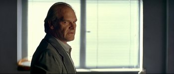 Movie still from “Bad Education” (2004), directed by Pedro Almodóvar – An older man in a gray suit looking at the camera; Close Up shot, Over the shoulder angle