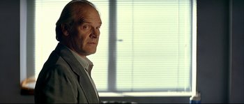 Movie still from “Bad Education” (2004), directed by Pedro Almodóvar – An older man in a gray suit standing in front of a window; Close Up shot, Low angle