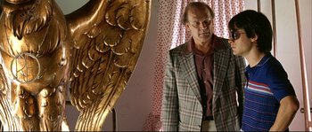 Movie still from “Bad Education” (2004), directed by Pedro Almodóvar – A man standing next to an angel statue; Medium shot, Low angle